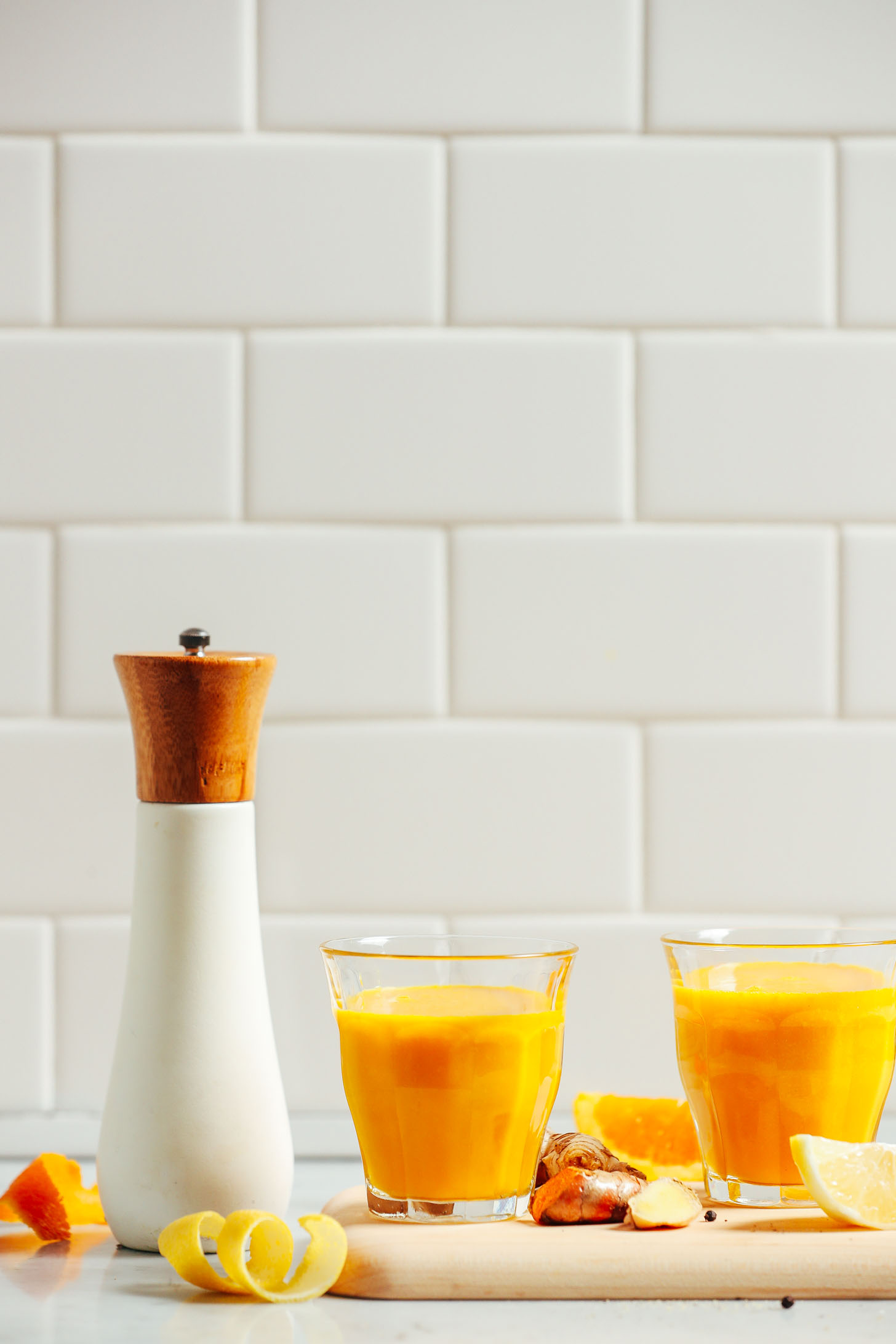 Glasses of our 5-Ingredient Turmeric Wellness Shots recipe surrounded by ingredients used to make them