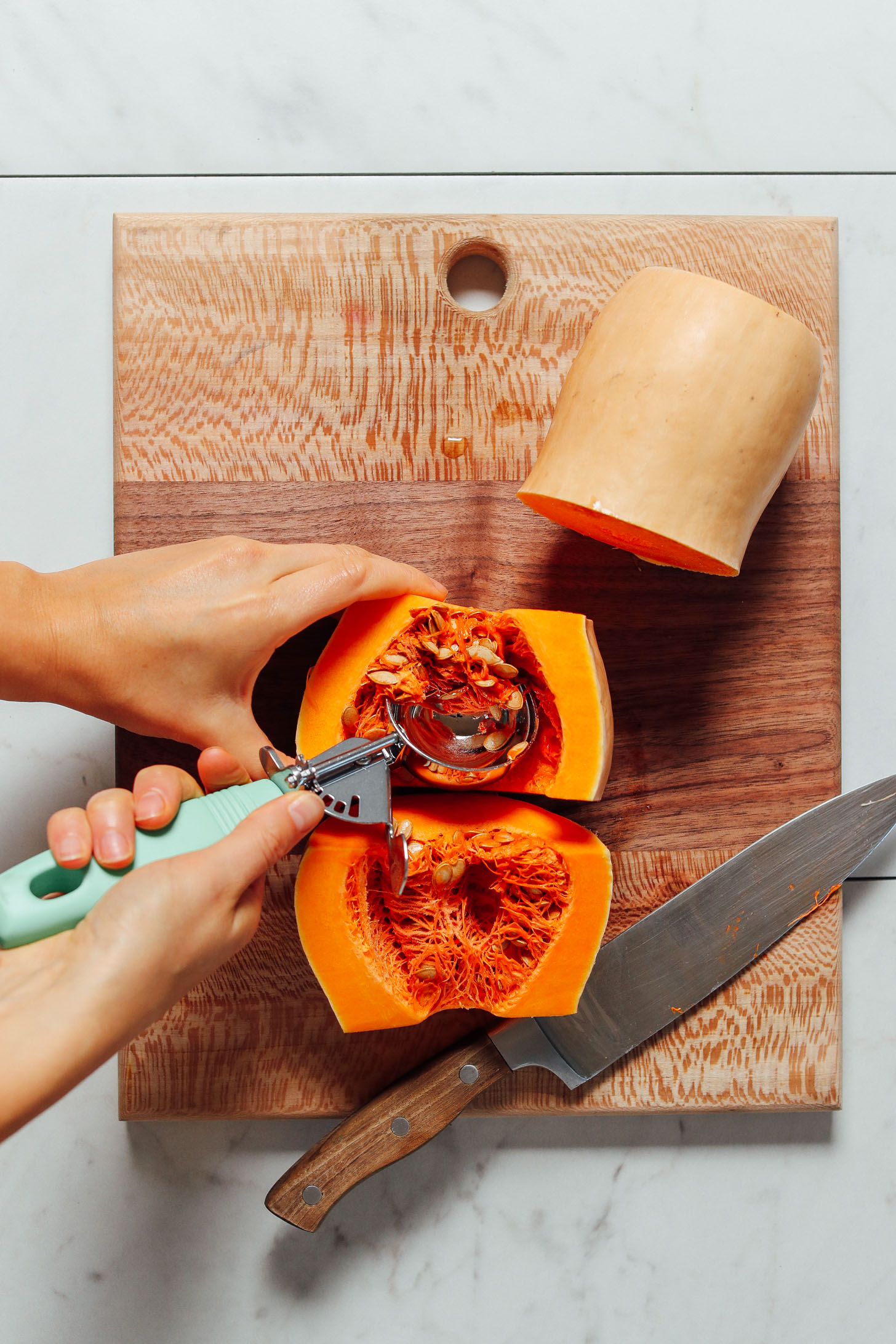 Using a cookie scooper to remove the seeds and flesh of a butternut squash