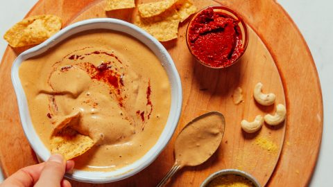 Overhead image of vegan cashew queso in a bowl with a hand dipping a dip