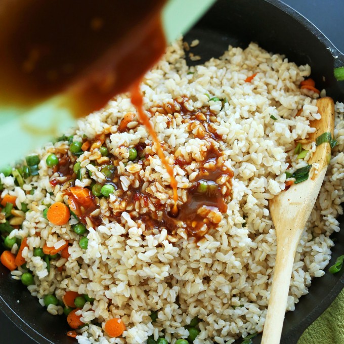 Pouring sauce into a pan of rice made with our How to Cook Brown Rice tutorial