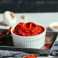 Harissa Paste in a white dish on a metal tray with garlic in the background
