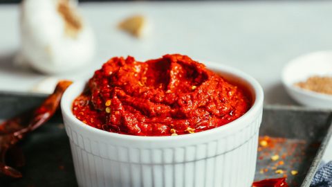 Harissa Paste in a white dish on a metal tray with garlic in the background