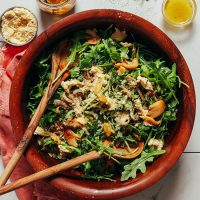 Salad spoons in a big wood bowl filled with Arugula Salad with Crispy Shallots