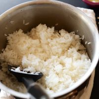 Backlit view of white rice cooked in a saucepan with a spatula scooping some rice