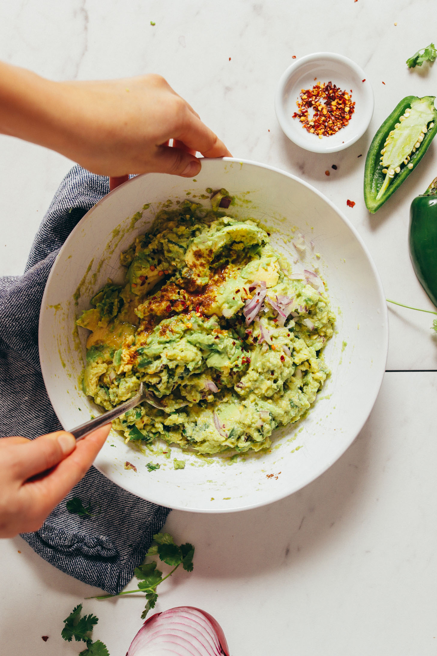 Overhead image of guacamole being stirred in a white bowl set over a blue towel