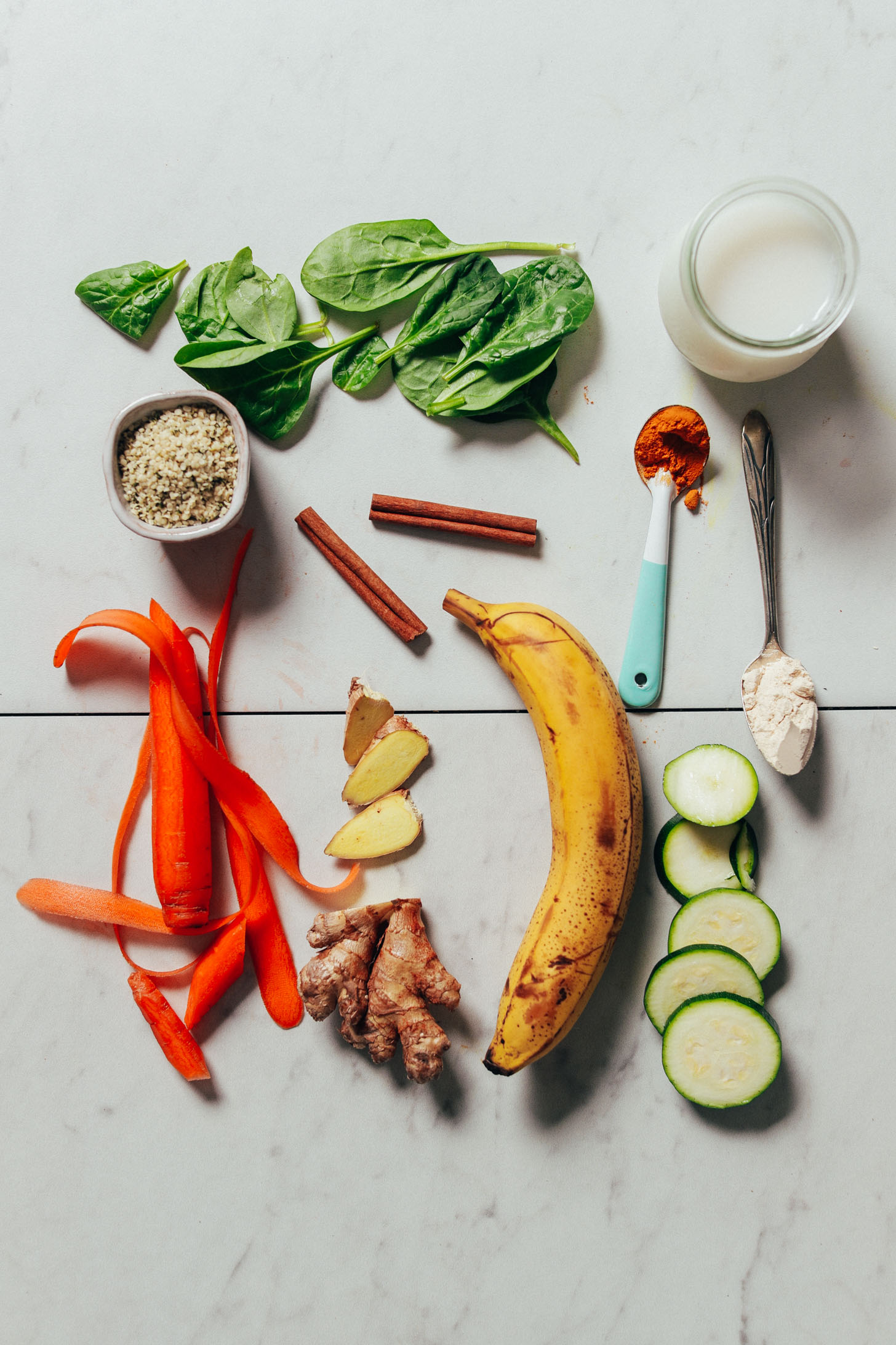 Overhead image of warming winter smoothie ingredients, including banana, spinach, zucchini, carrot, and protein powder