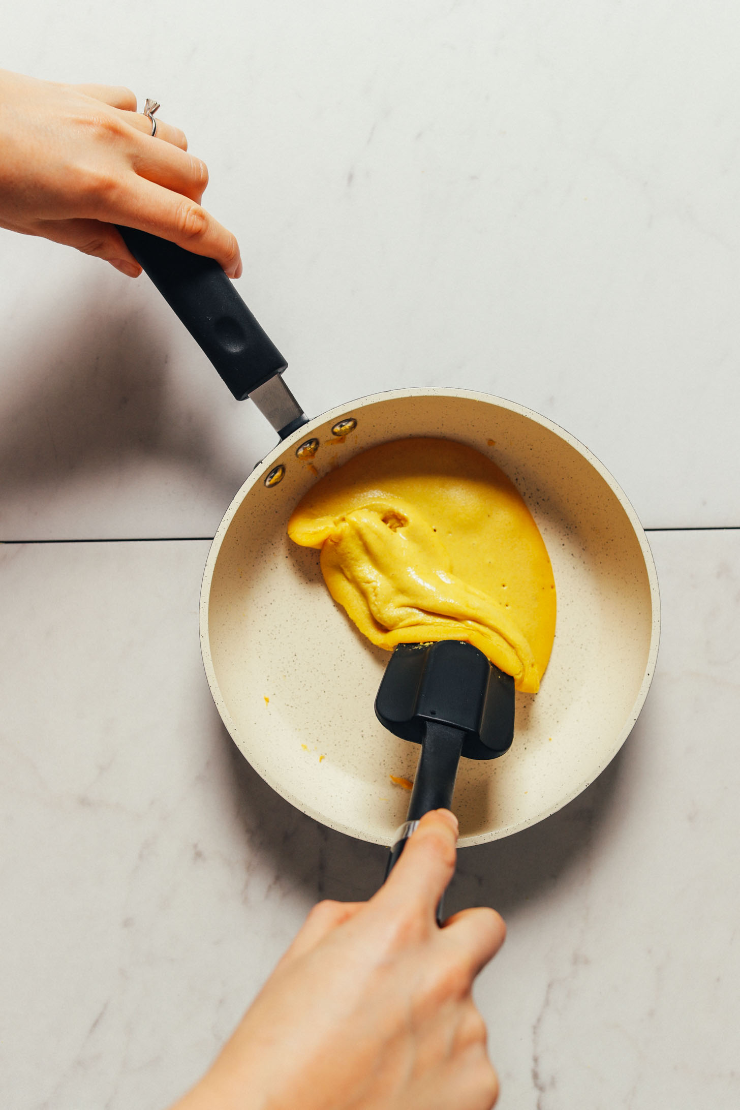Using a rubber spatula to cook a vegan egg in a nonstick pan