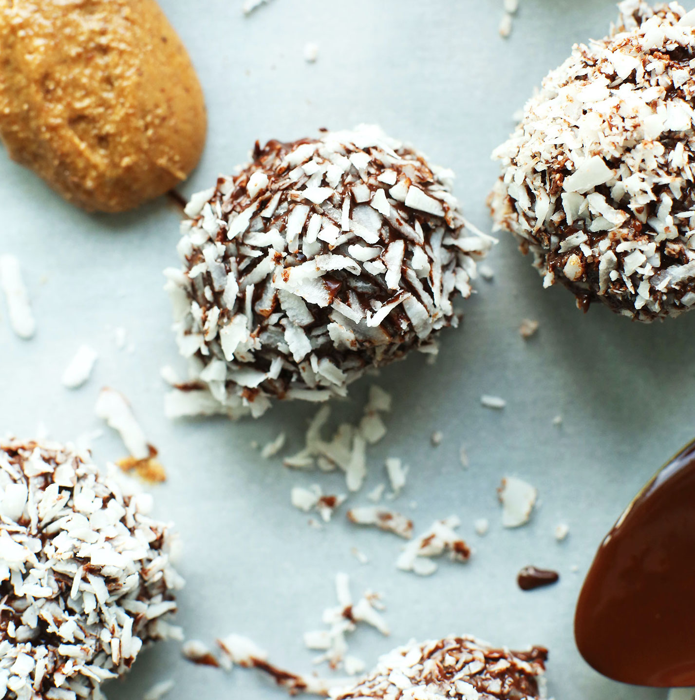 Spoonfuls of almond butter and dark chocolate beside Vegan Chocolate Snowballs made with dates