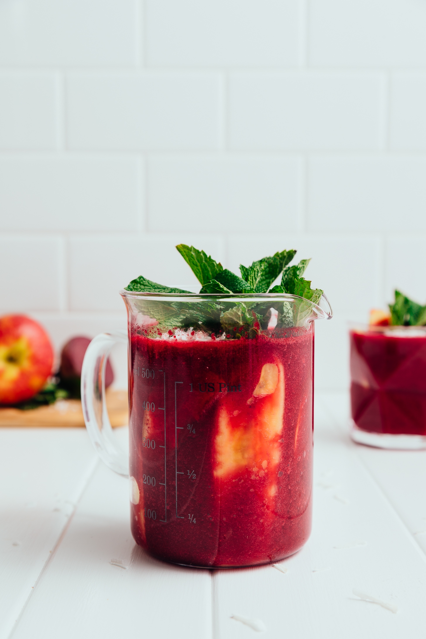 Measuring glass filled with our Beet and Berry Smoothie recipe topped with fresh mint