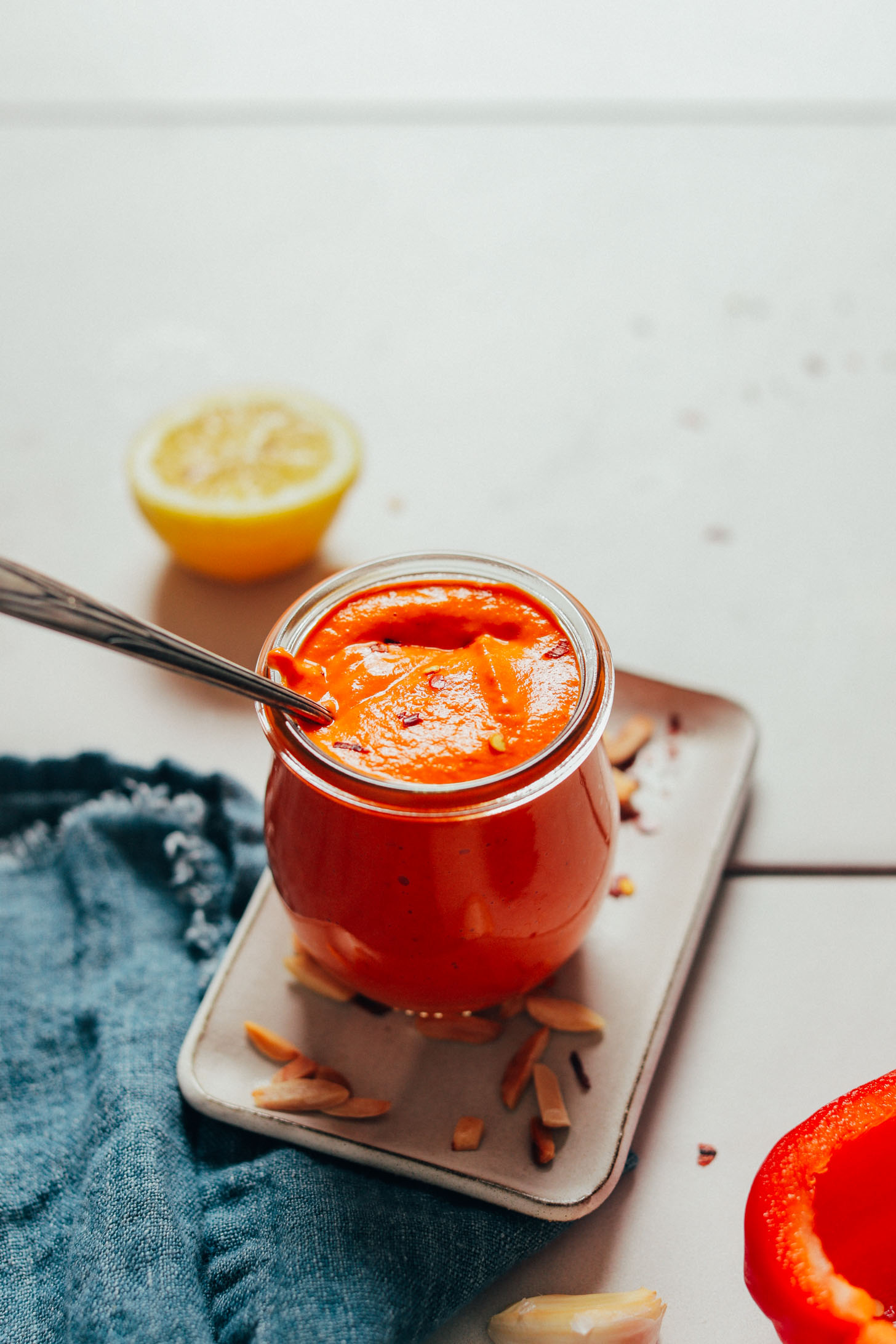 Spoon submerged in a jar of Creamy Romesco Sauce made with toasted almonds, lemon, and red bell pepper