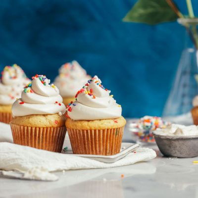 Plate of vanilla cupcakes topped with Vegan Buttercream Frosting and rainbow sprinkles