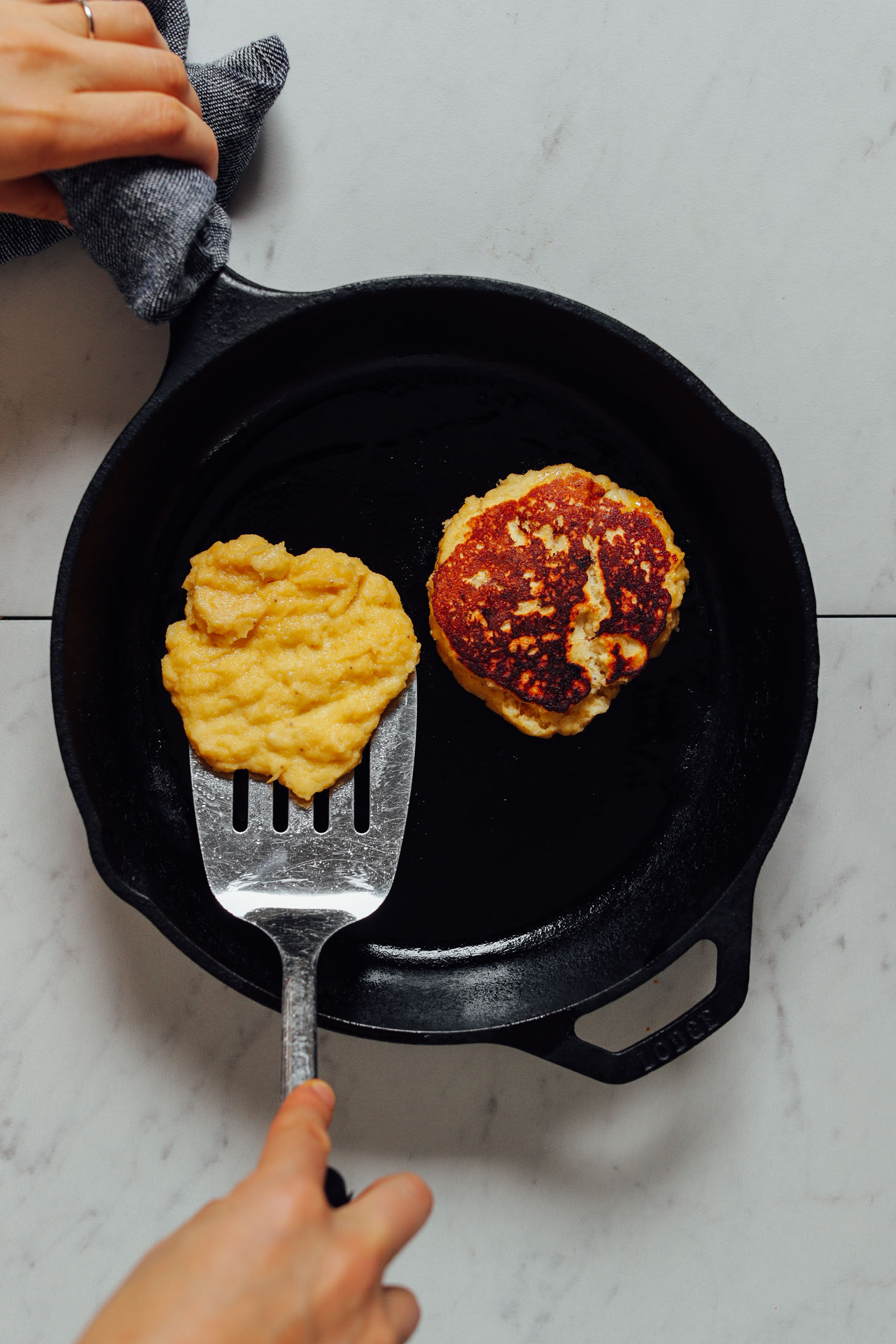Using a metal spatula to flip a Banana Egg Pancake in a cast-iron skillet