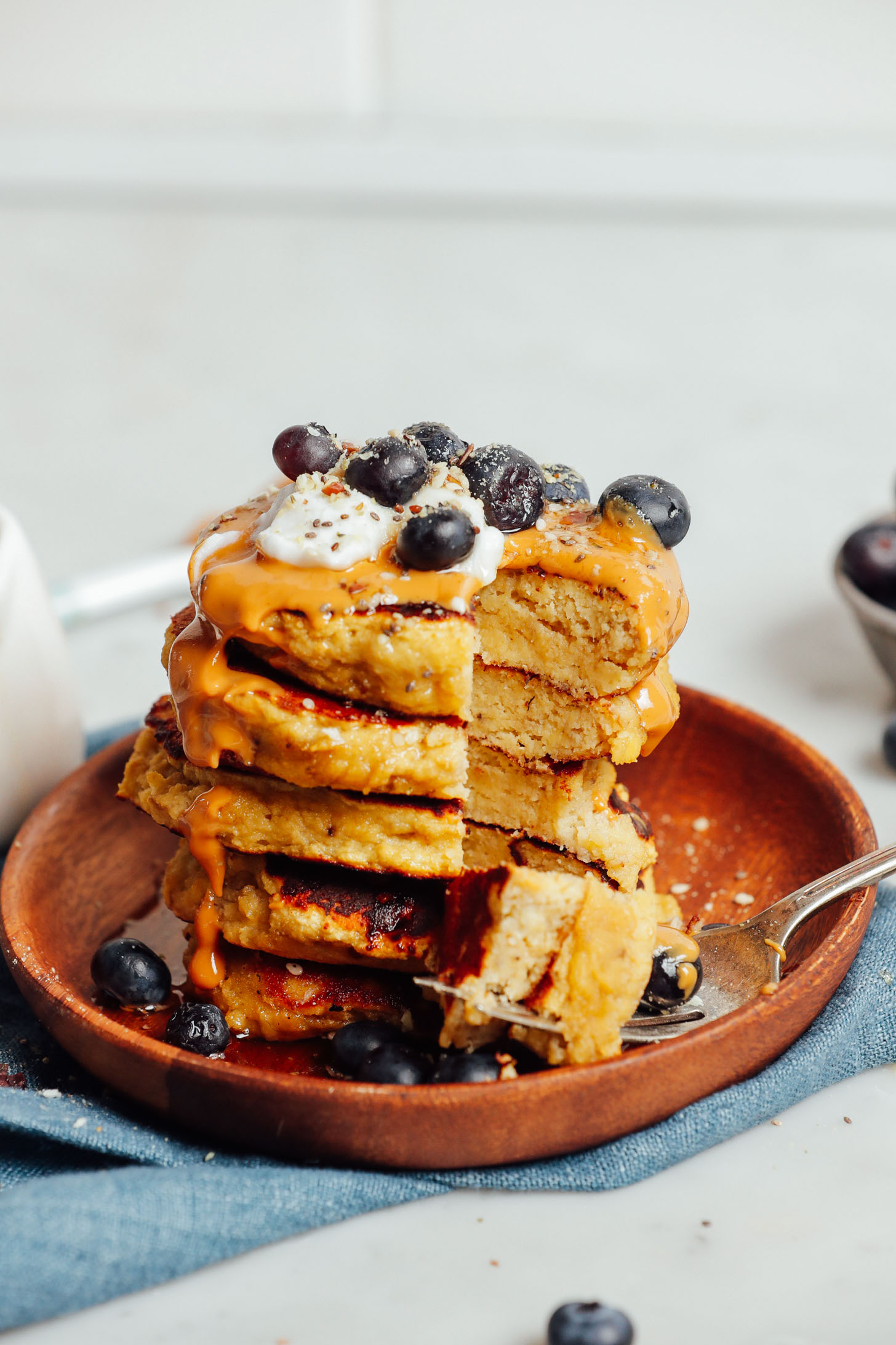 Wood plate with a stack of fluffy grain-free Banana Pancakes with a bite resting on a fork