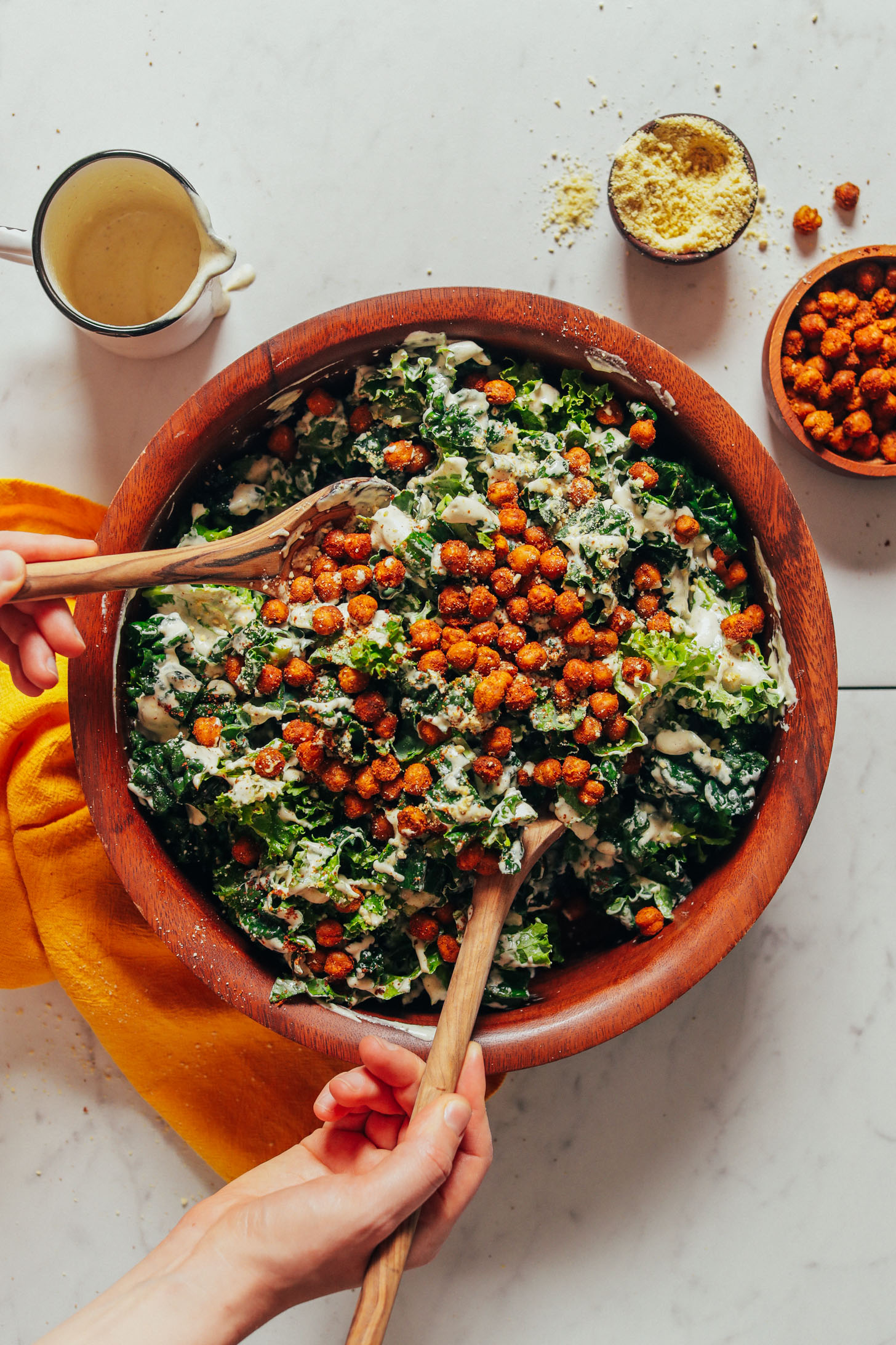 Using wooden salad spoons to toss a bowl of Chickpea Kale Salad topped with tandoori chickpeas