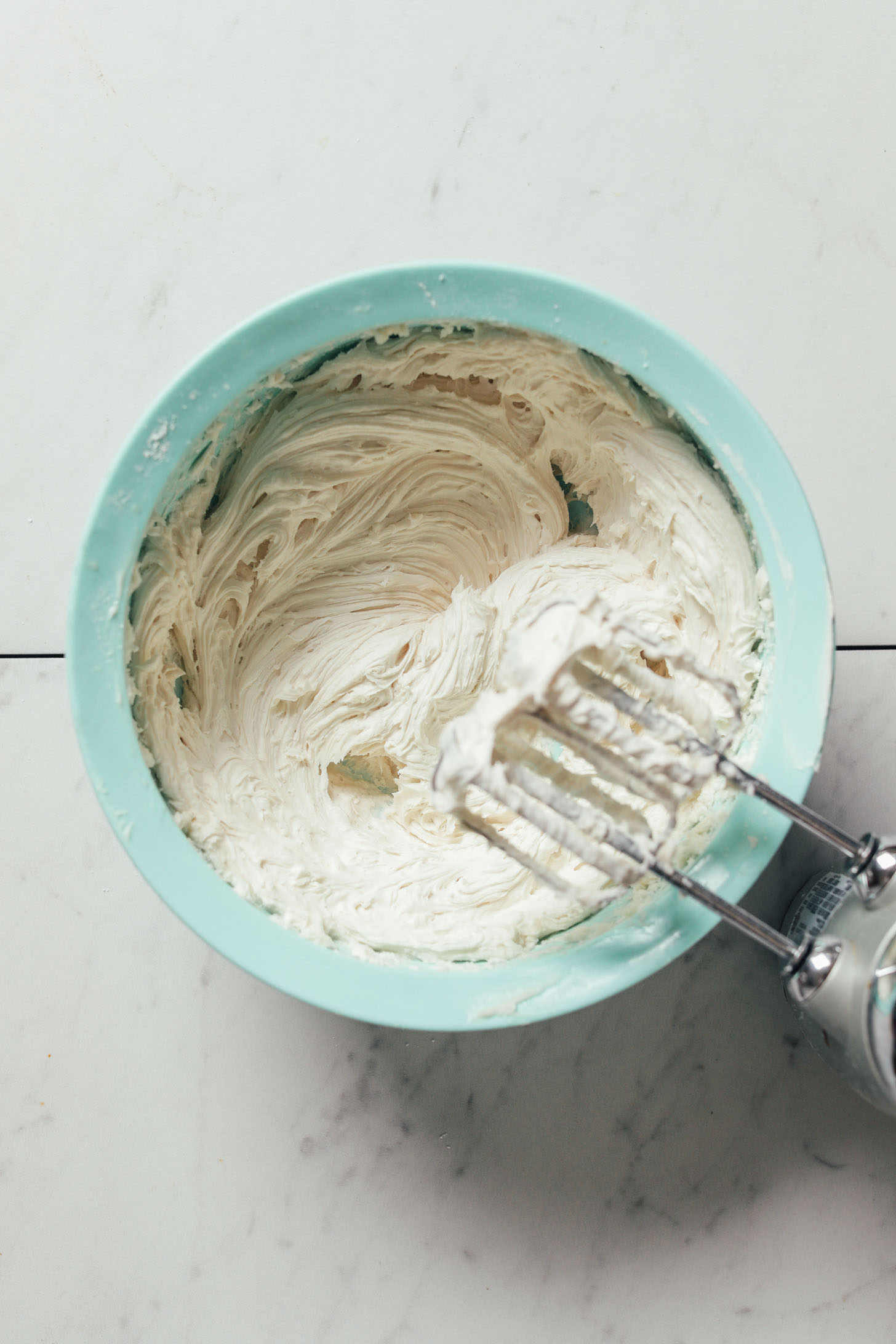 Electric hand mixer resting above a bowl of simple homemade Vegan Buttercream Frosting