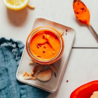 Jar and spoonful of easy homemade Romesco Sauce surrounded by ingredients used to make it