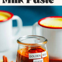 Jar of golden milk paste next to two mugs of golden milk