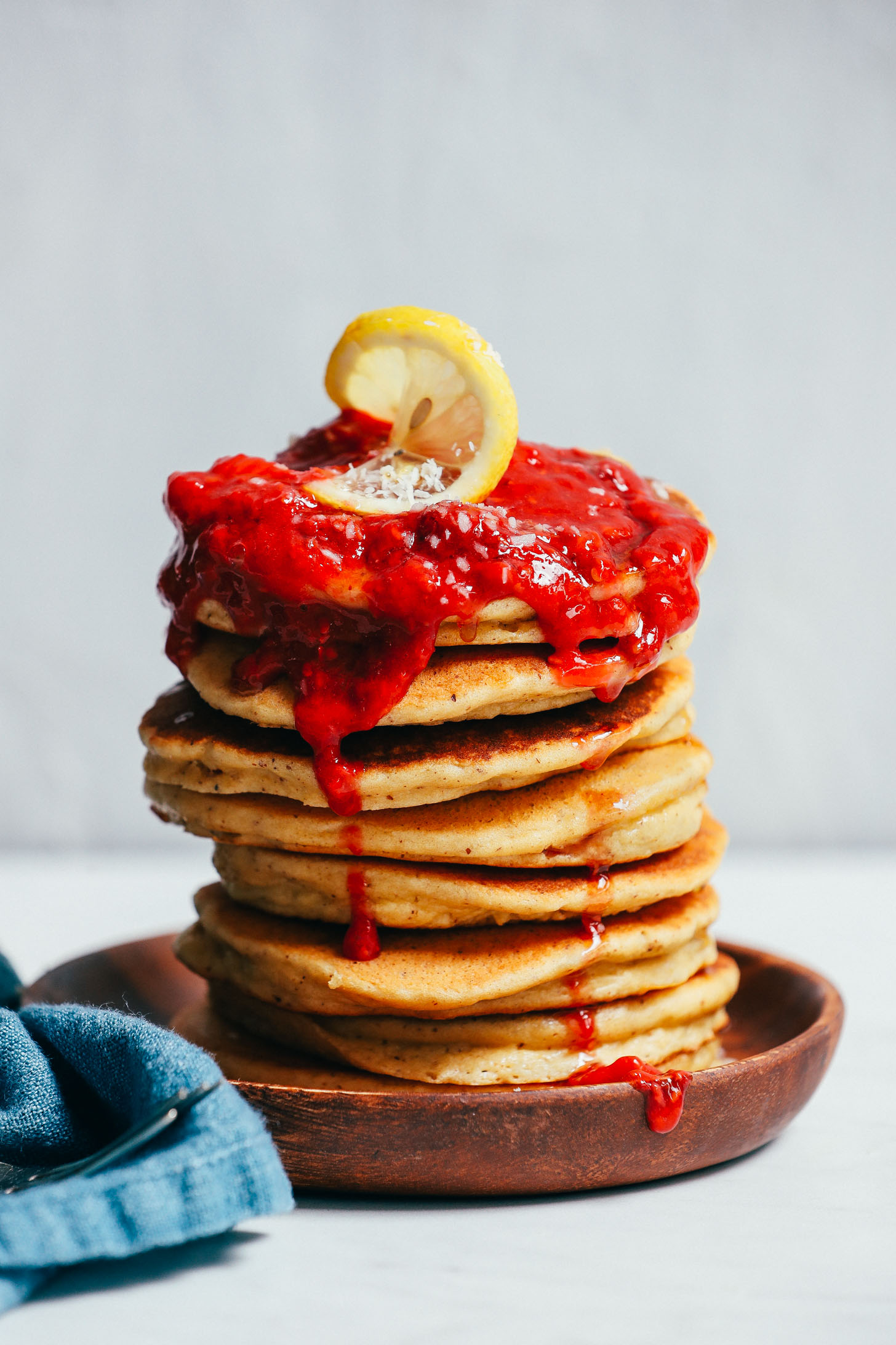 Stack of fluffy Grain-Free Pancakes topped with raspberry compote and a lemon slice