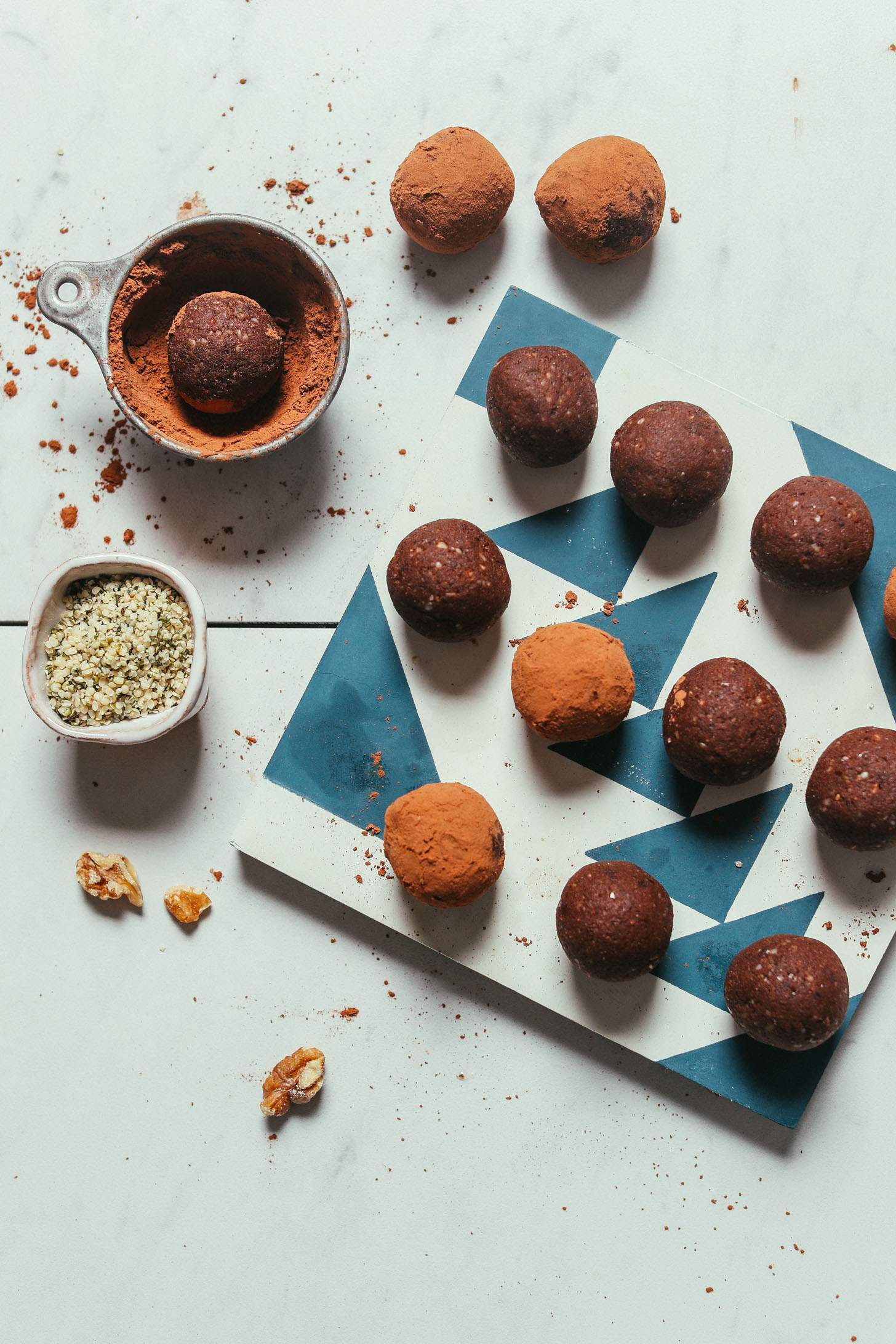 Tile with Brownie Bliss Balls beside measuring cups of hemp seeds and cacao powder for rolling