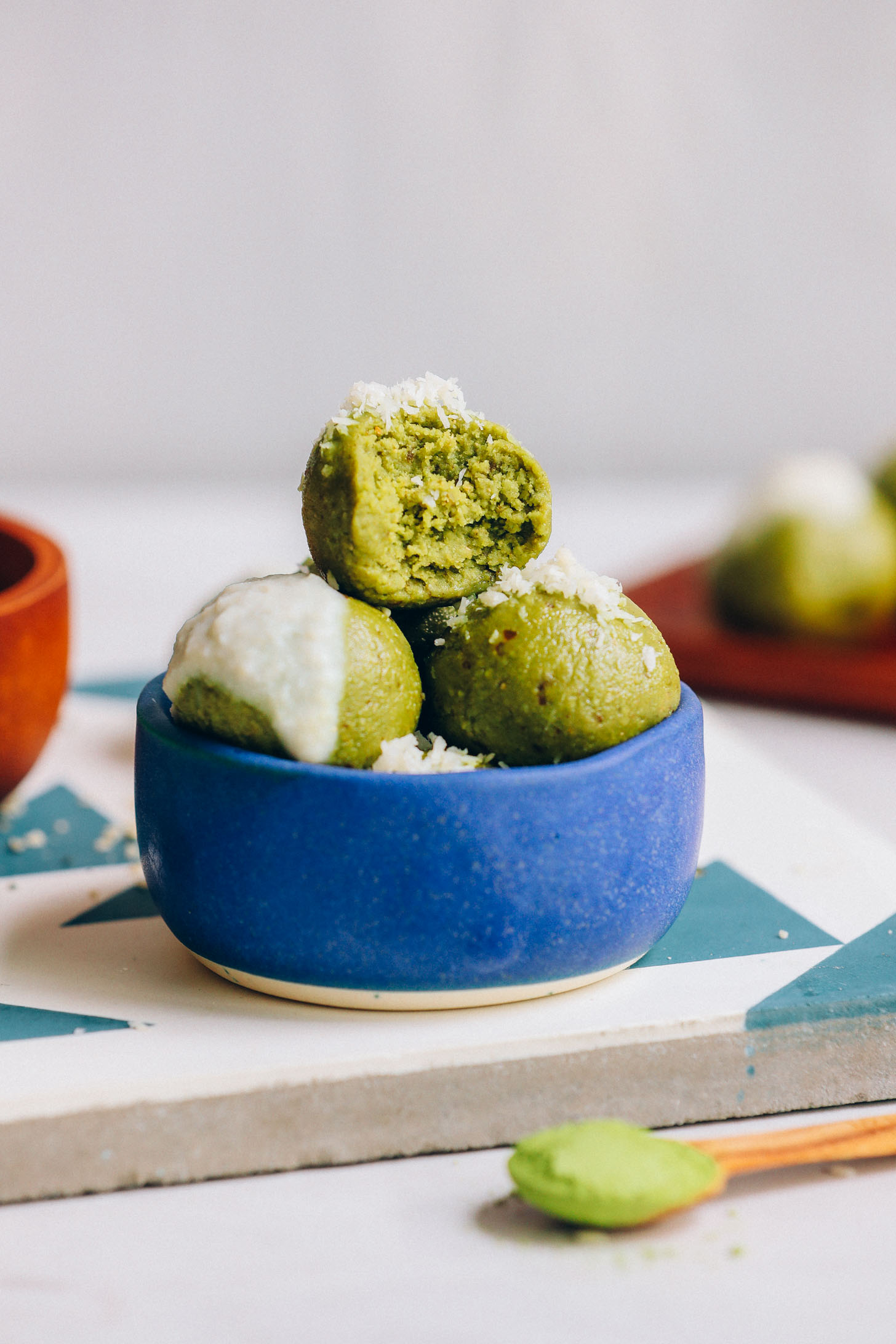 Bowl of vegan Matcha Bliss Balls topped with shredded coconut and coconut butter icing