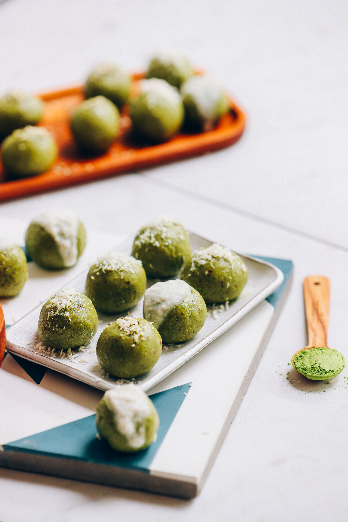 Wood and ceramic plates filled with Matcha Bliss Balls for a low sugar, date-sweetened energy boost