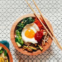 Chopsticks resting on a bowl of Bibimbap made with brown rice and lots of veggies
