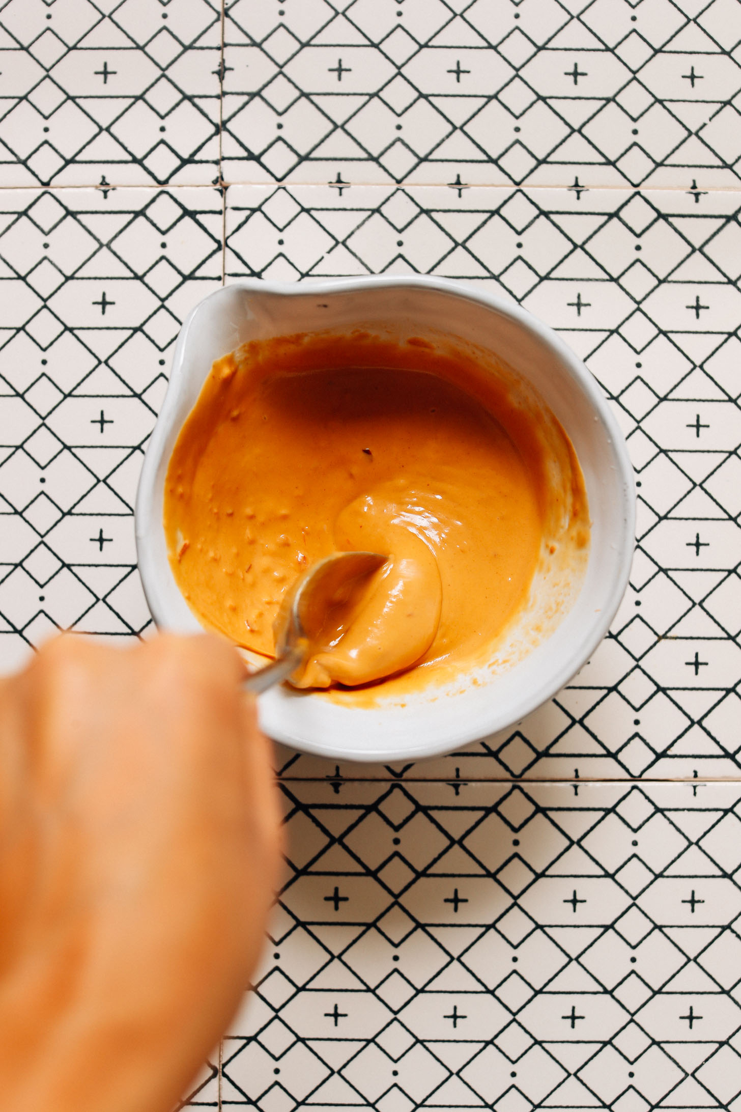 Using a spoon to stir a bowl of Spicy Peanut Sauce for topping Gado Gado