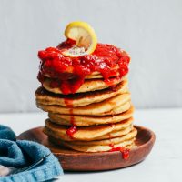 Stack of Grain-Free Pancakes topped with raspberry compote and a lemon slice