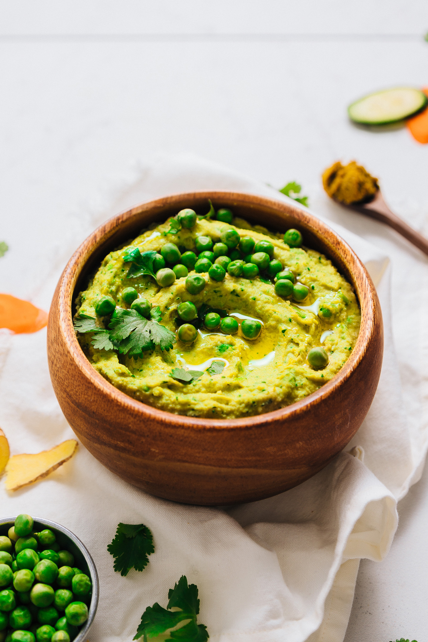 Wood bowl filled with Curry Hummus topped with green peas