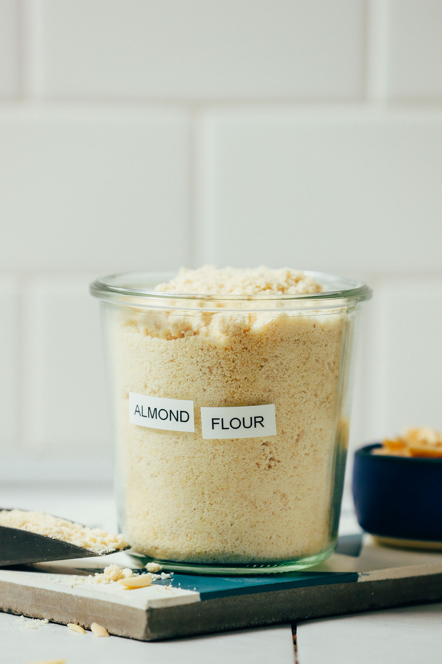 Jar of almond flour sitting beside a bowl of blanched almonds