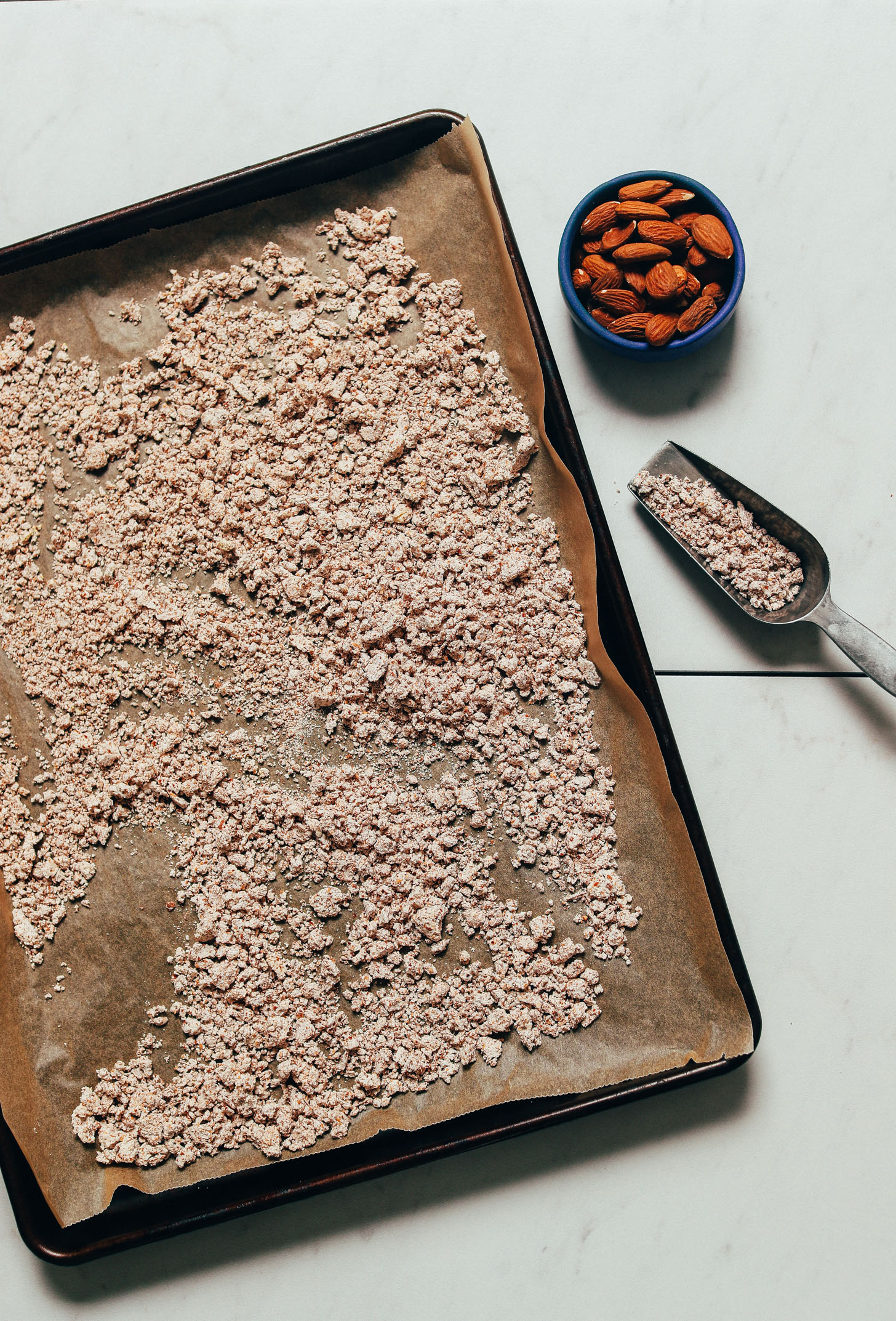 Parchment-lined baking sheet filled with dried almond pulp for making homemade almond meal from almond pulp