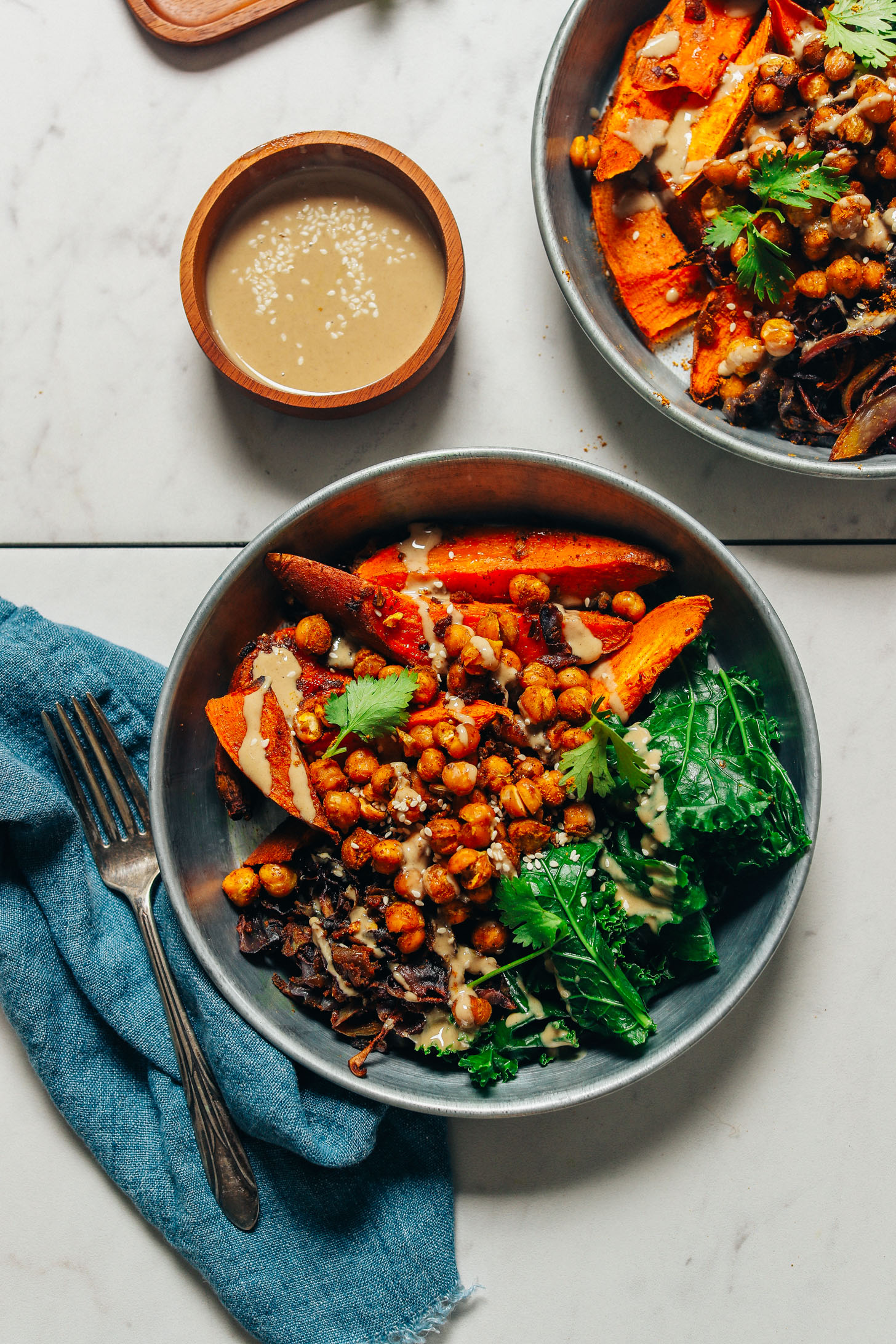 Bowl of tahini sauce beside bowls of our Sweet Potato Sheet Pan Dinner for a simple and delicious meal