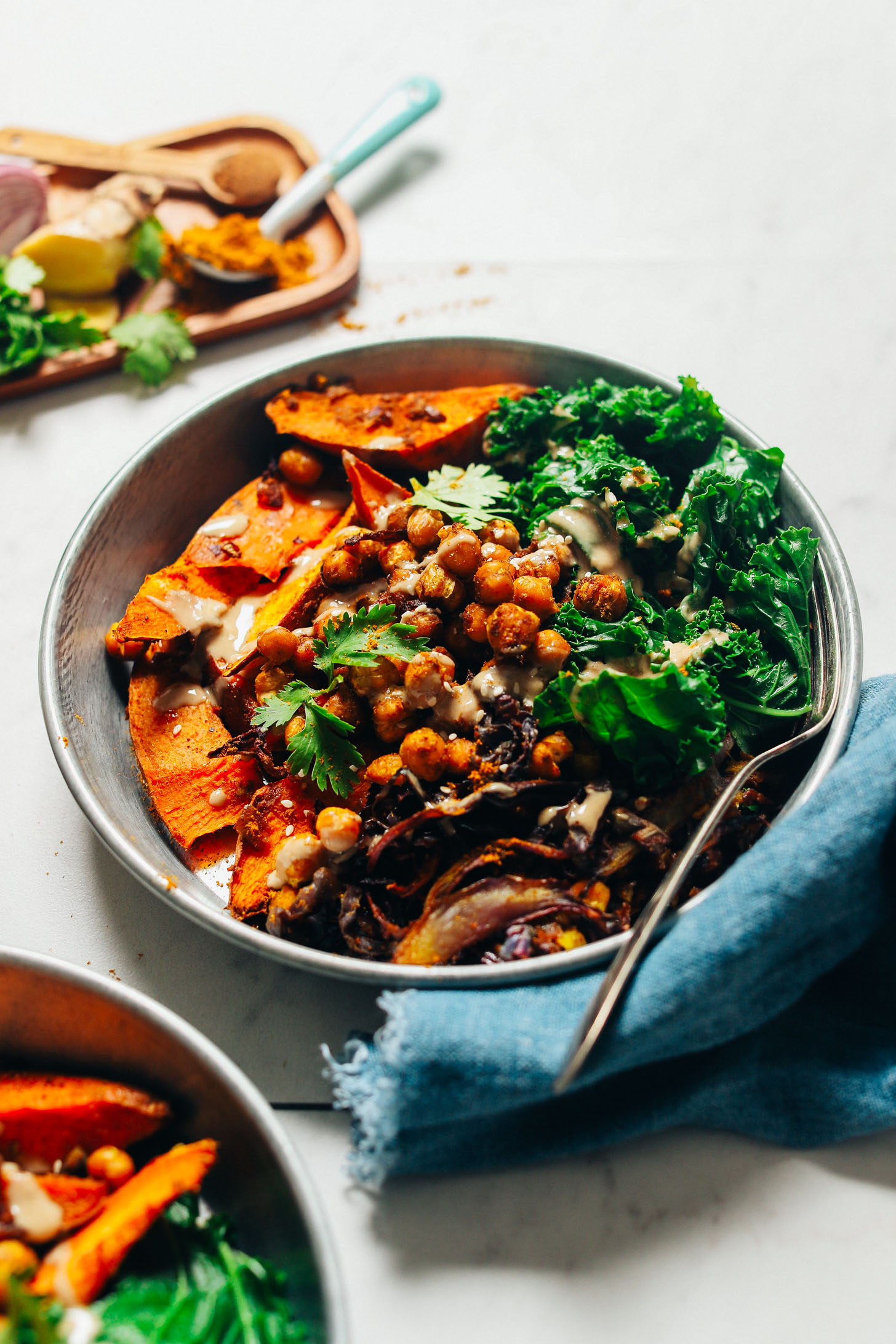 Bowls filled with steamed kale, tahini sauce, and our Sweet Potato Sheet Pan Dinner recipe