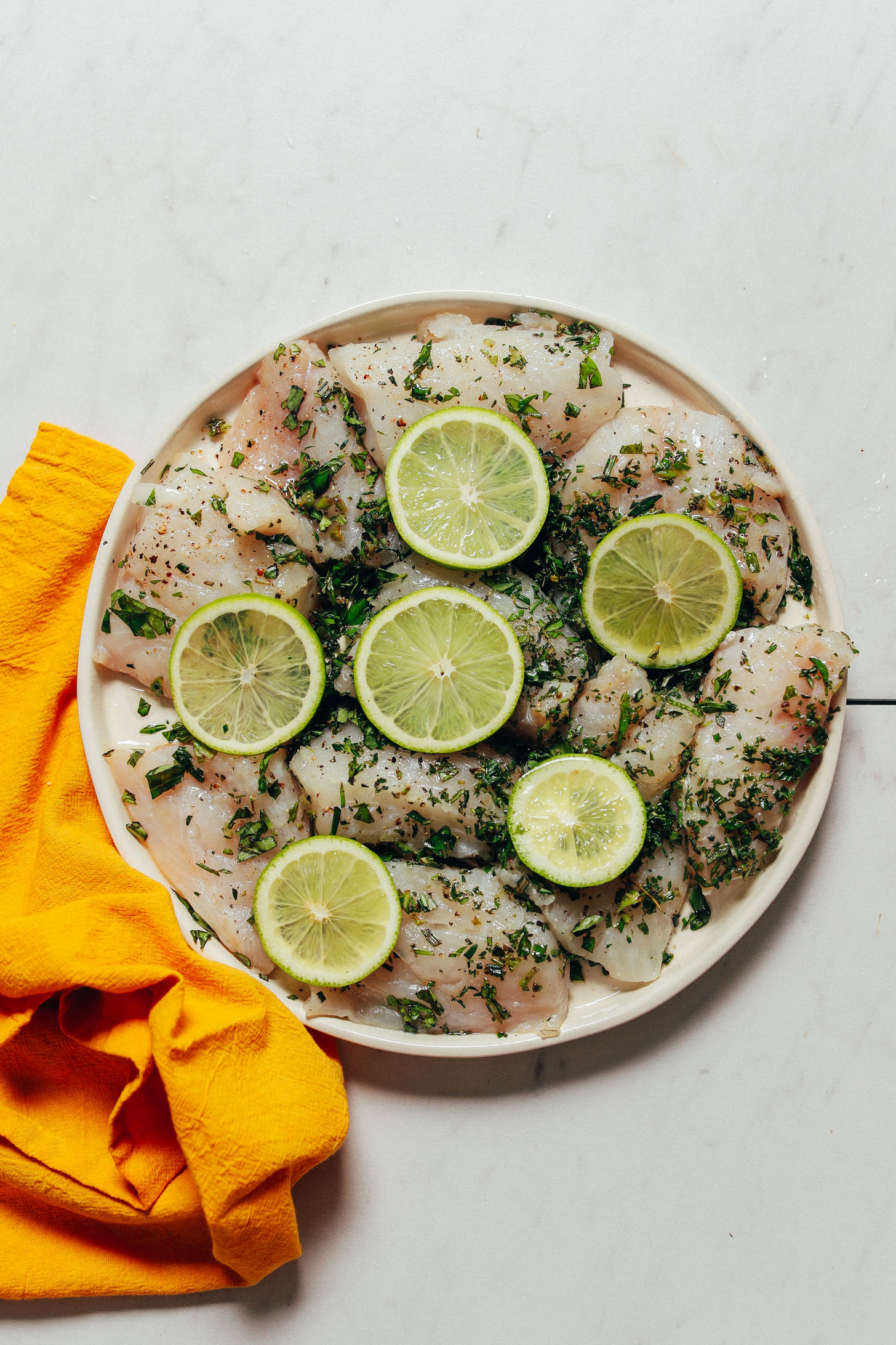 Plate of white fish coated with fresh herbs and lime slices for a delicious summer fish recipe