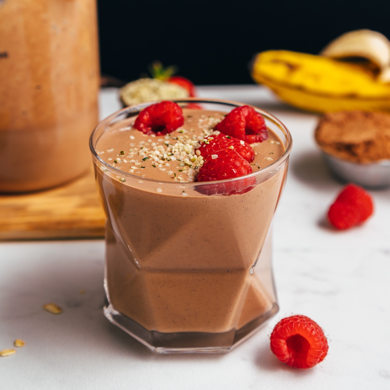 Glass of our plant-based Chocolate Protein Shake topped with fresh raspberries and hemp seeds