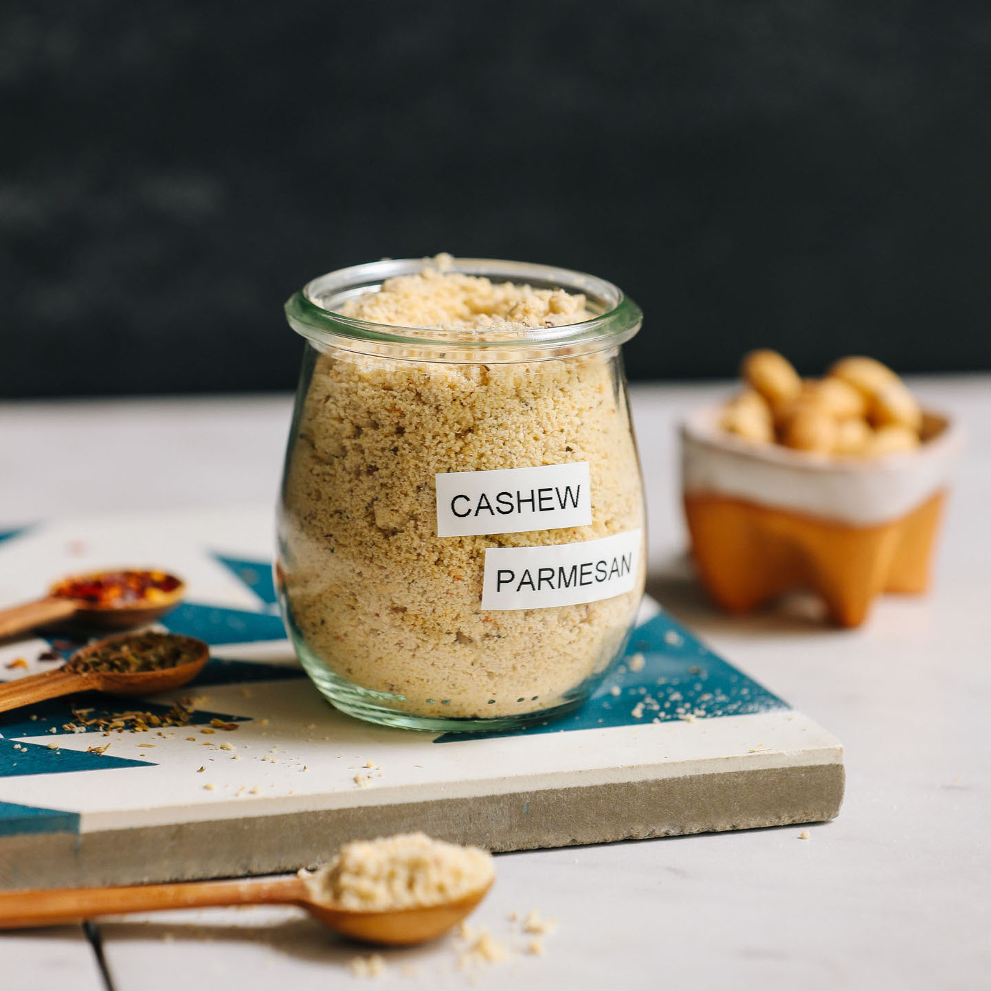 Jar of yeast-free Vegan Parmesan Cheese beside cashews and spices to make it
