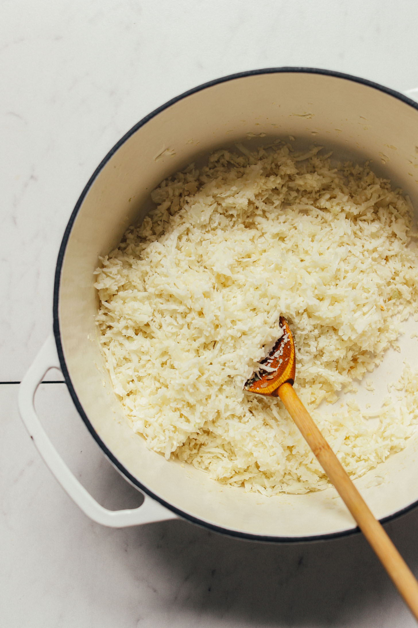 Using a wooden spoon to stir cauliflower rice in a large dutch oven