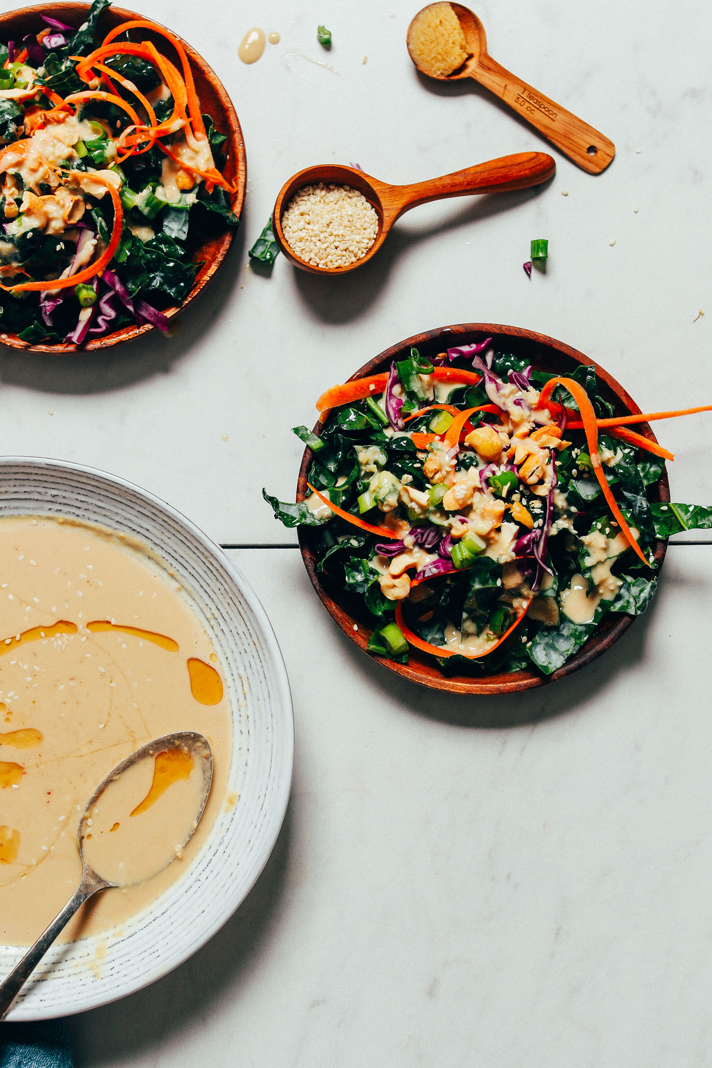 Plates of kale, carrot, and cabbage salad beside a bowl of our Ginger Garlic Miso Tahini Dressing