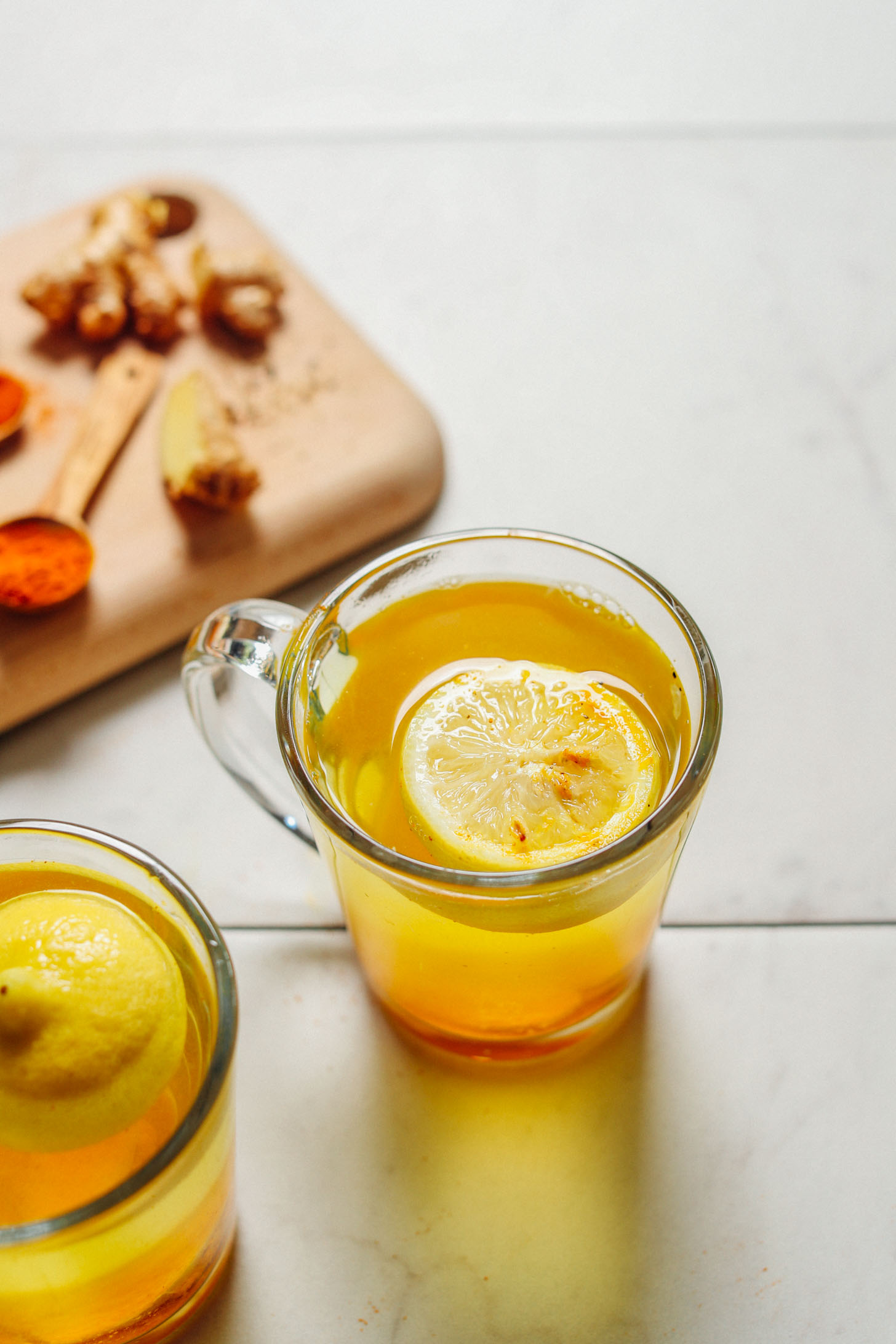 image of lemon ginger water at a 45 degree angle in a clear mug with spoonfuls of spices behind it