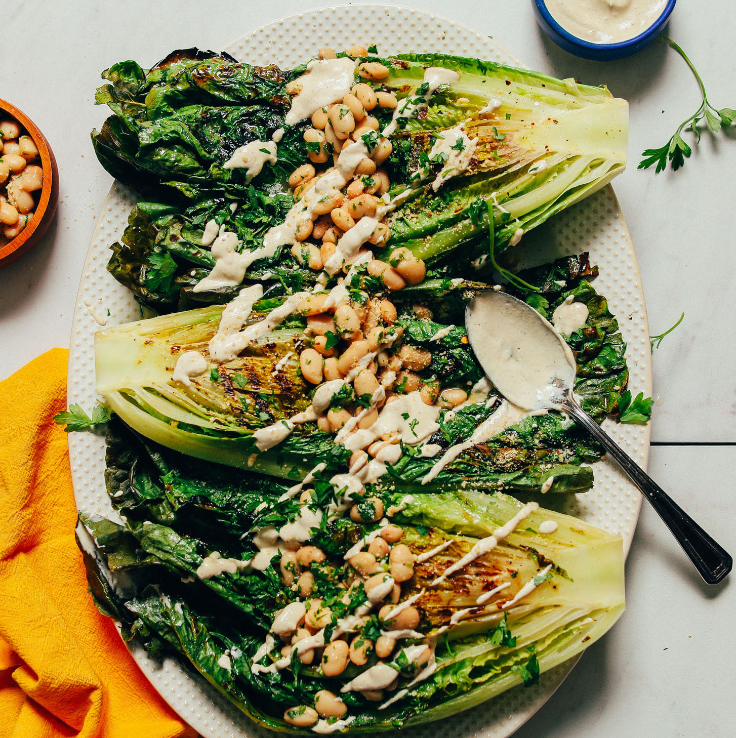 A platter of grilled romaine salad with lemon herbed beans and a drizzle of vegan Caesar dressing.
