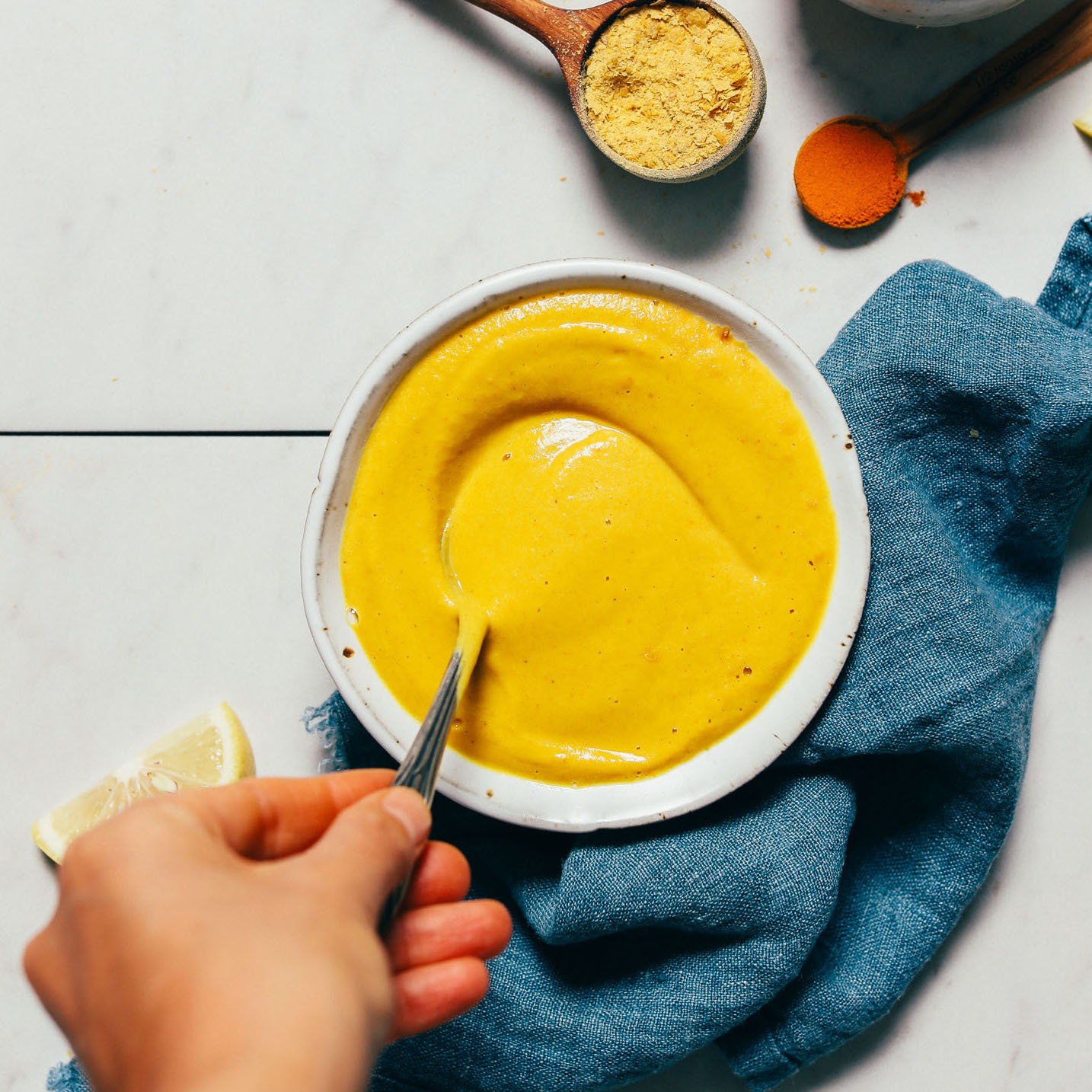 Stirring a bowl of bright yellow sauce made from chickpeas, turmeric, nutritional yeast, and more