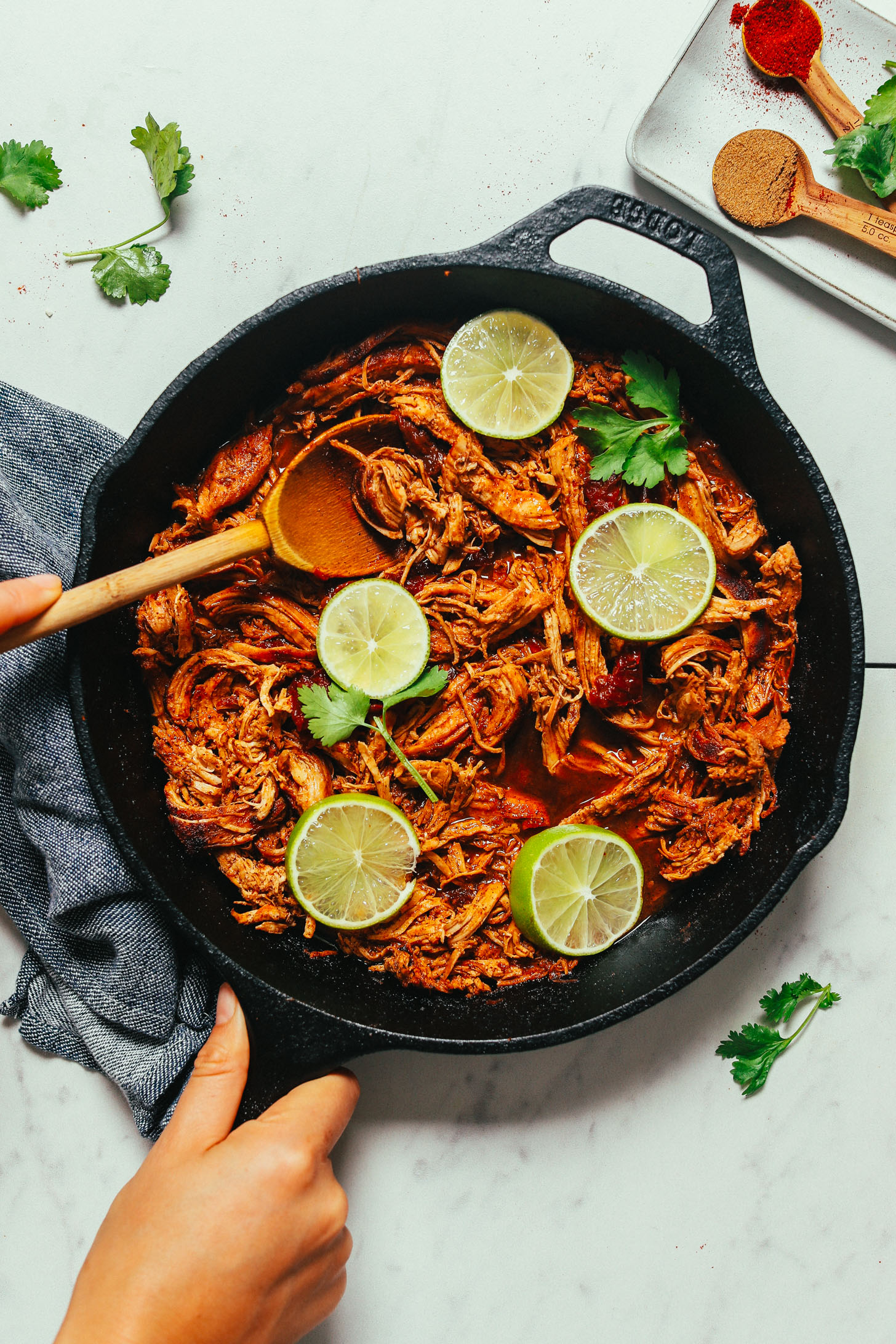 Wooden spoon in a skillet of Mexican Shredded Chicken topped with cilantro and limes