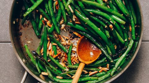 Using a wooden spoon to stir a pot of Garlic Green Beans for a Thanksgiving side