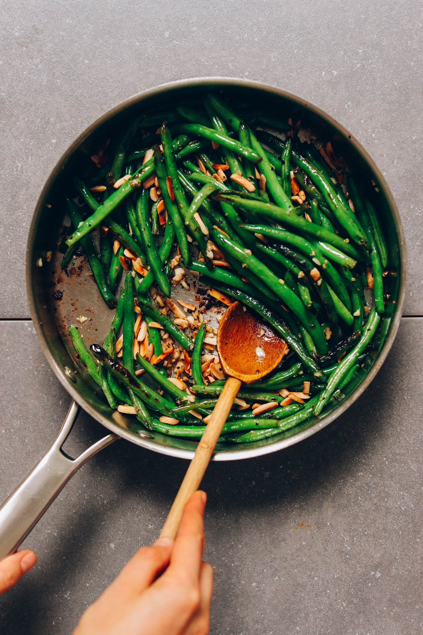Using a wooden spoon to stir a pan of Green Beans with Toasted Slivered Almonds