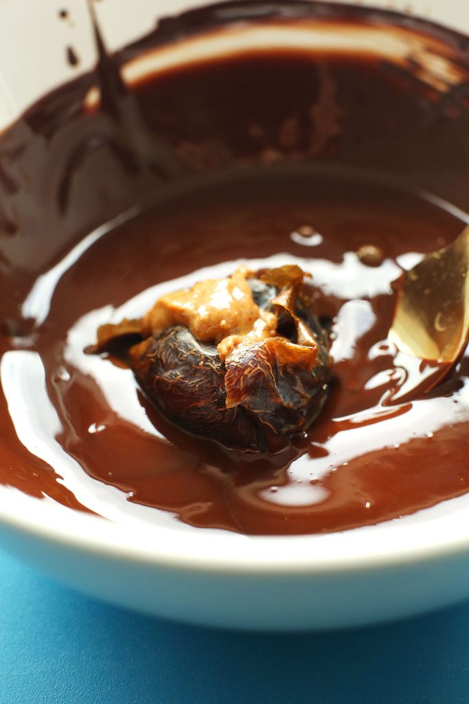 Almond butter stuffed date in a bowl of melted dark chocolate for our Vegan Chocolate Snowball recipe