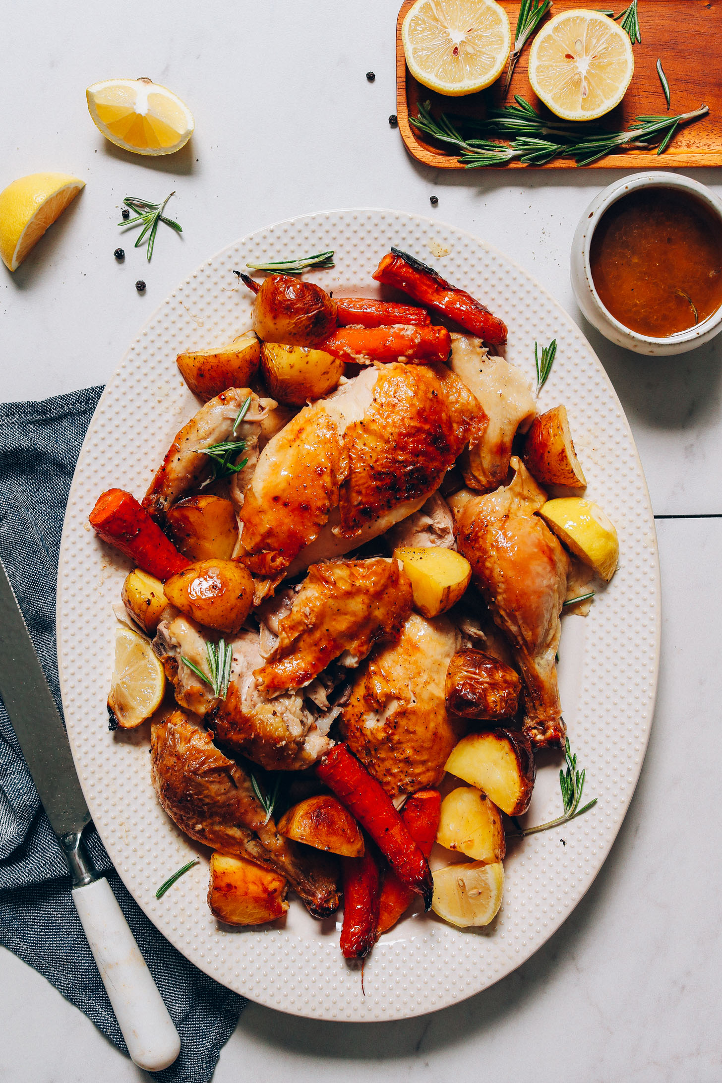 Large platter filled with Roasted Chicken and Vegetables beside gravy, lemons, and rosemary