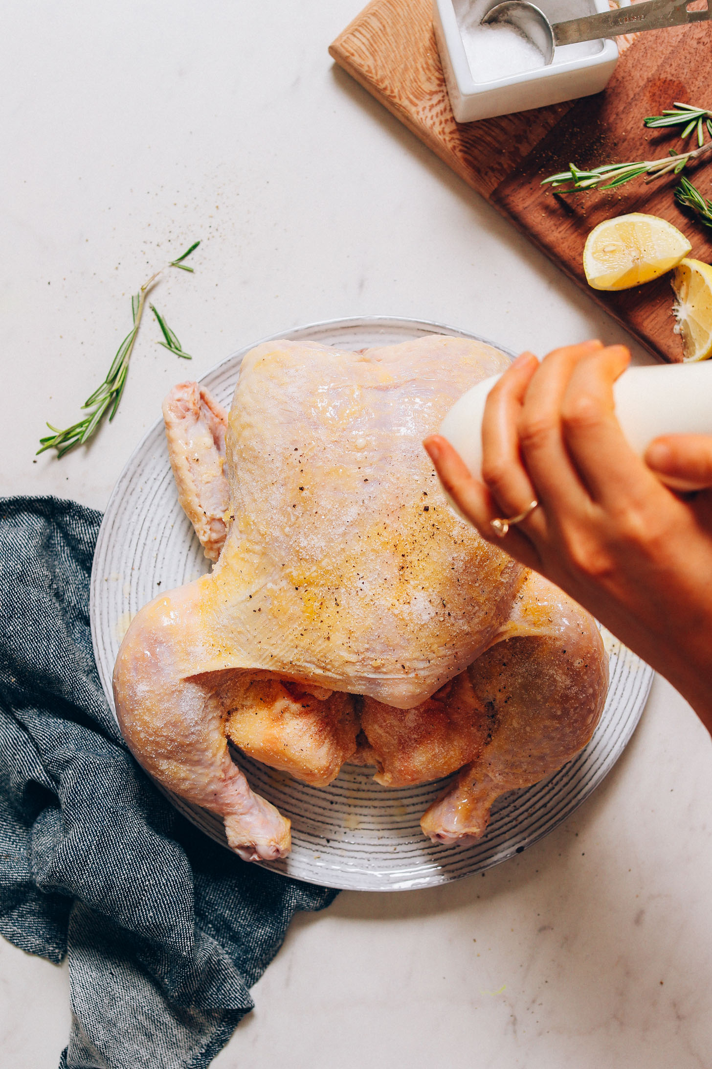 Sprinkling black pepper onto a chicken to make our delicious Oven Roasted Chicken recipe