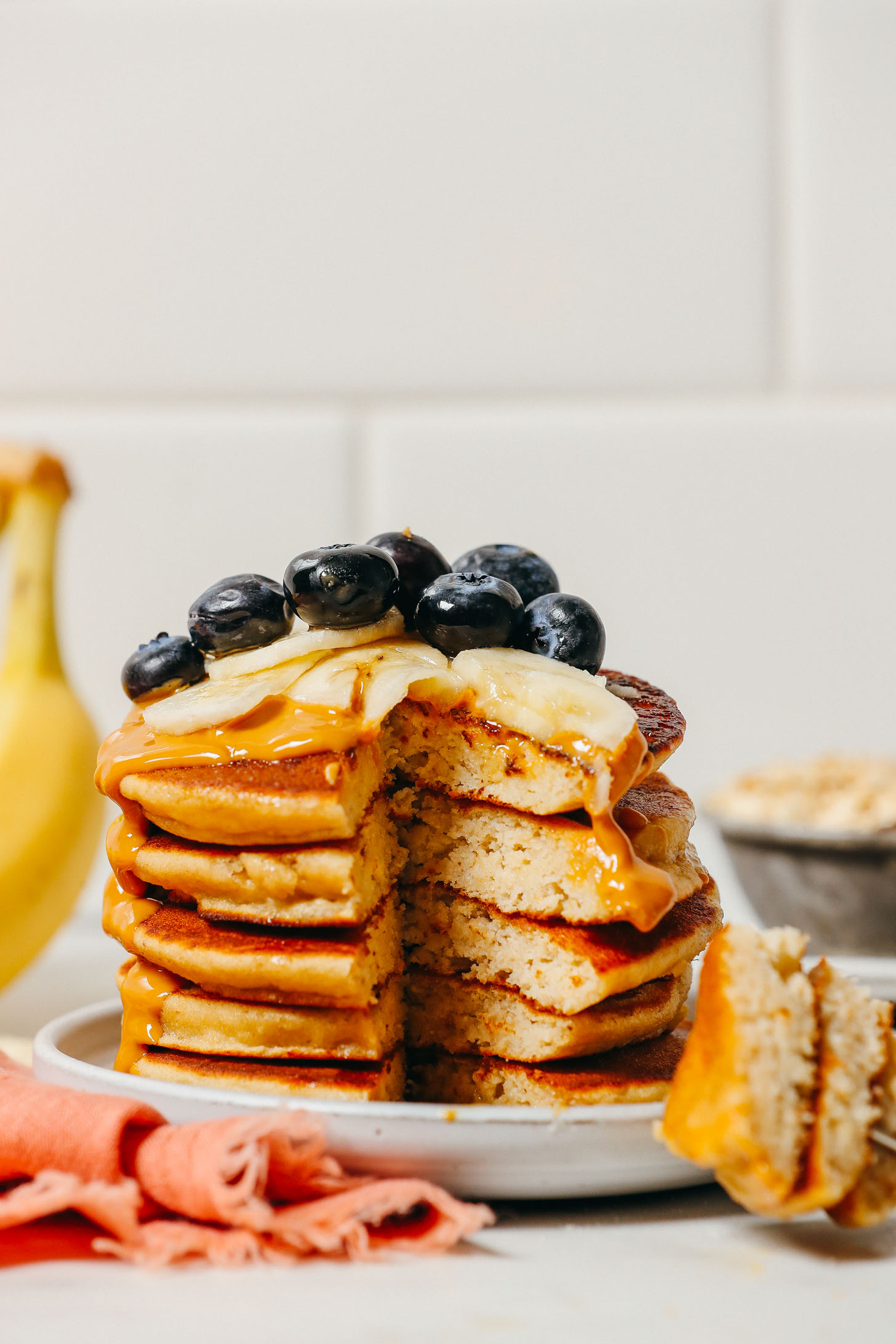 Sliced removed from a stack of Banana Pancakes topped with peanut butter and fresh fruit