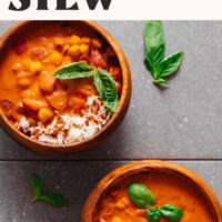 Two bowls of West African-inspired chickpea tomato peanut stew served with rice and fresh basil