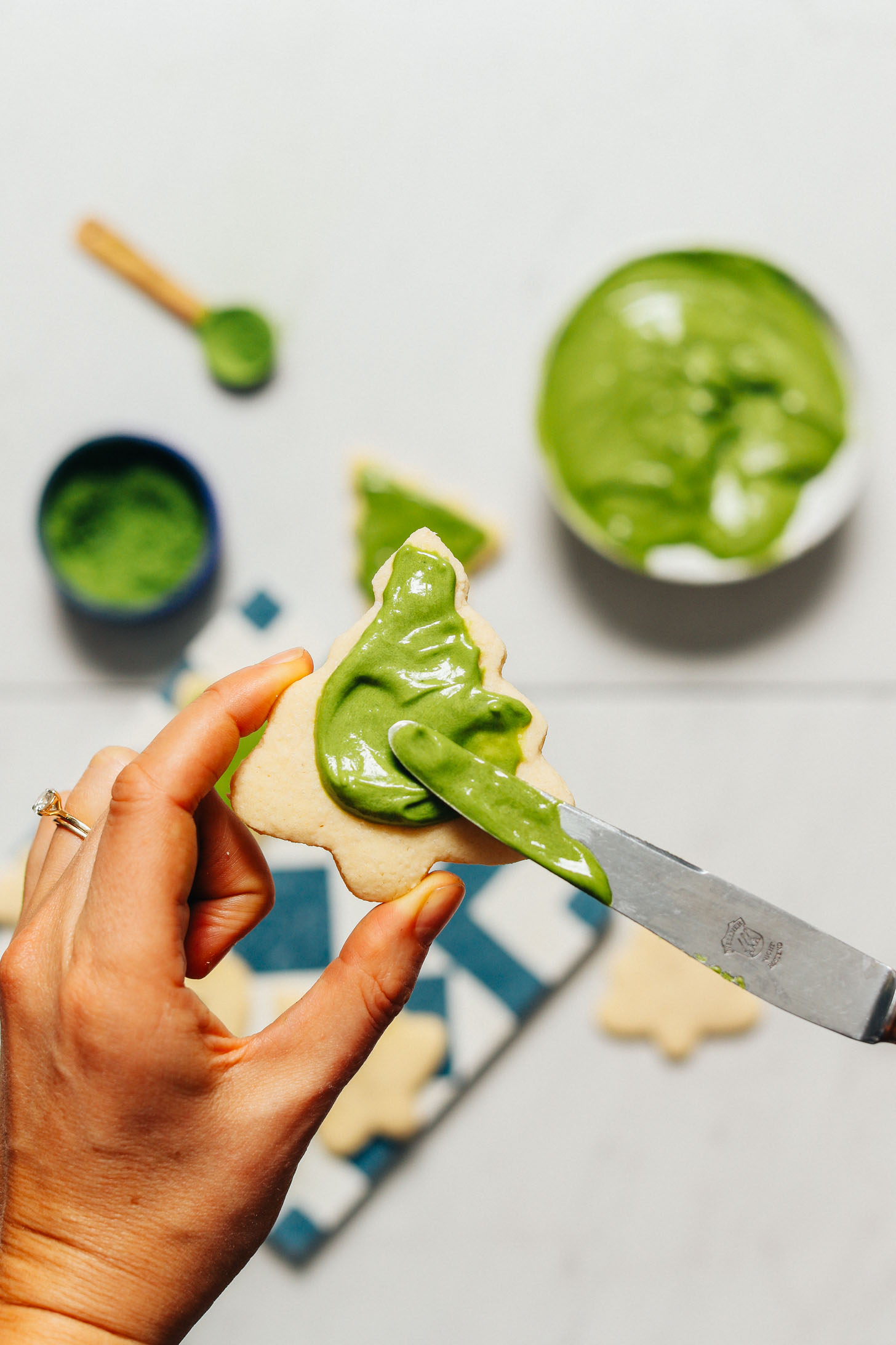 Spreading matcha frosting onto a grain-free Christmas sugar cookie